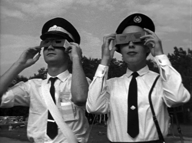 A man and a women in uniform stand holding special glasses over their eyes to safely observe a social eclipse.