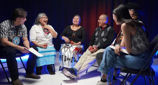 A group of Indigenous Elders and youth seated in a semi-circle and laughing